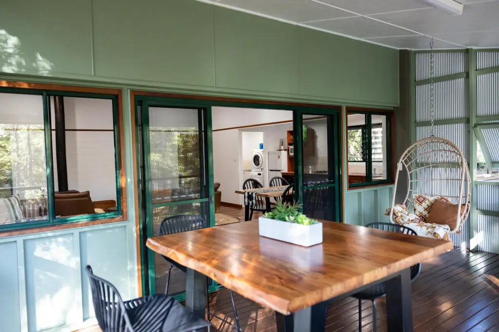 Wooden dining table and chairs on a covered timber deck overlooking a rainforest backdrop at Palmerston Cottage.