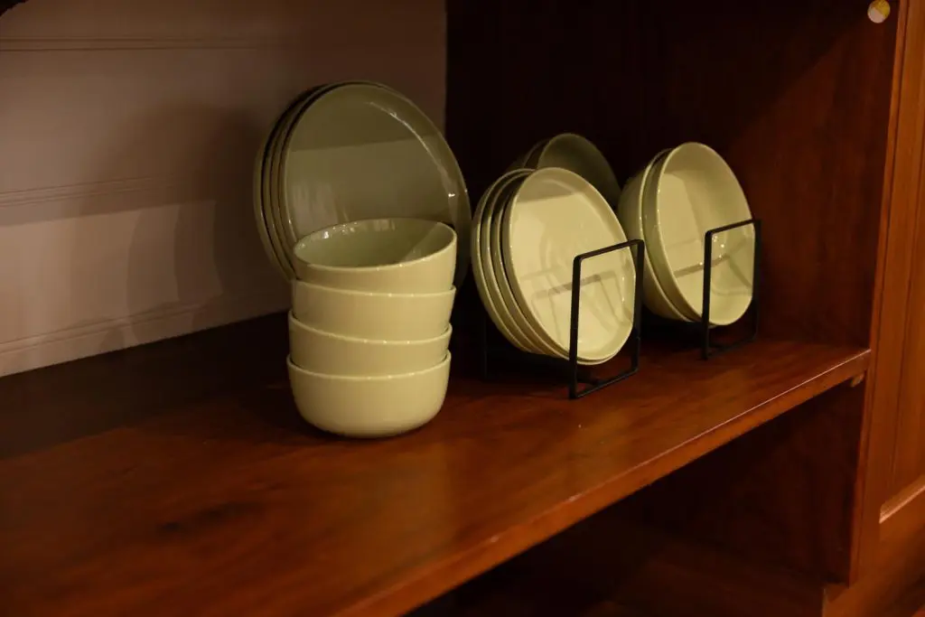 Stacks of light green ceramic bowls and matching plates neatly arranged on a dark timber cabinet shelf inside Palmerston Cottage.