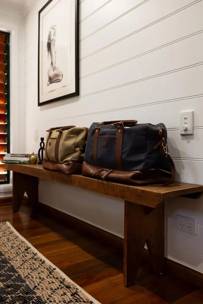 Leather duffel bags set on a rustic timber bench beneath a framed art print.