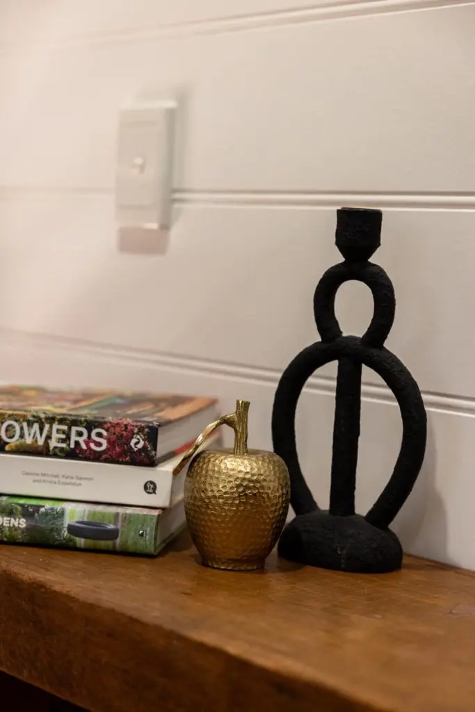Black sculptural metal candle holder and brass decorative apple sitting next to stacked coffee table books on a wooden surface.