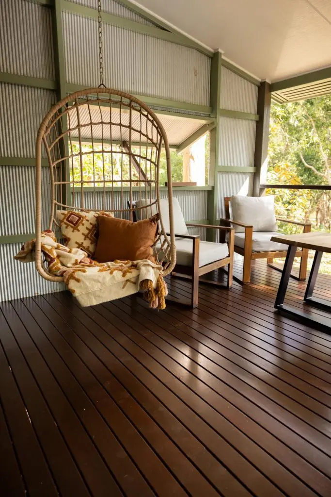 Suspended rattan hanging swing chair with throw pillows and blanket set on a timber deck at Palmerston Cottage.